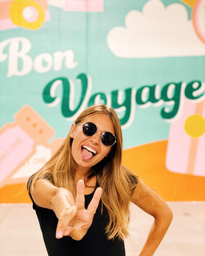 An influencer poses in front of a mural that reads Bon Voyage